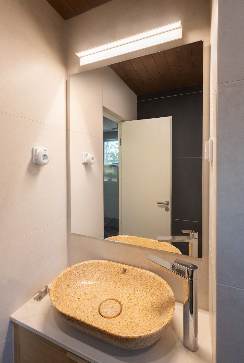 In una piccola toilette, una lampada da parete bianca minimalista lunga 60 centimetri illumina elegantemente lo specchio. La luce ha una temperatura di colore di 3 000 Kelvin.